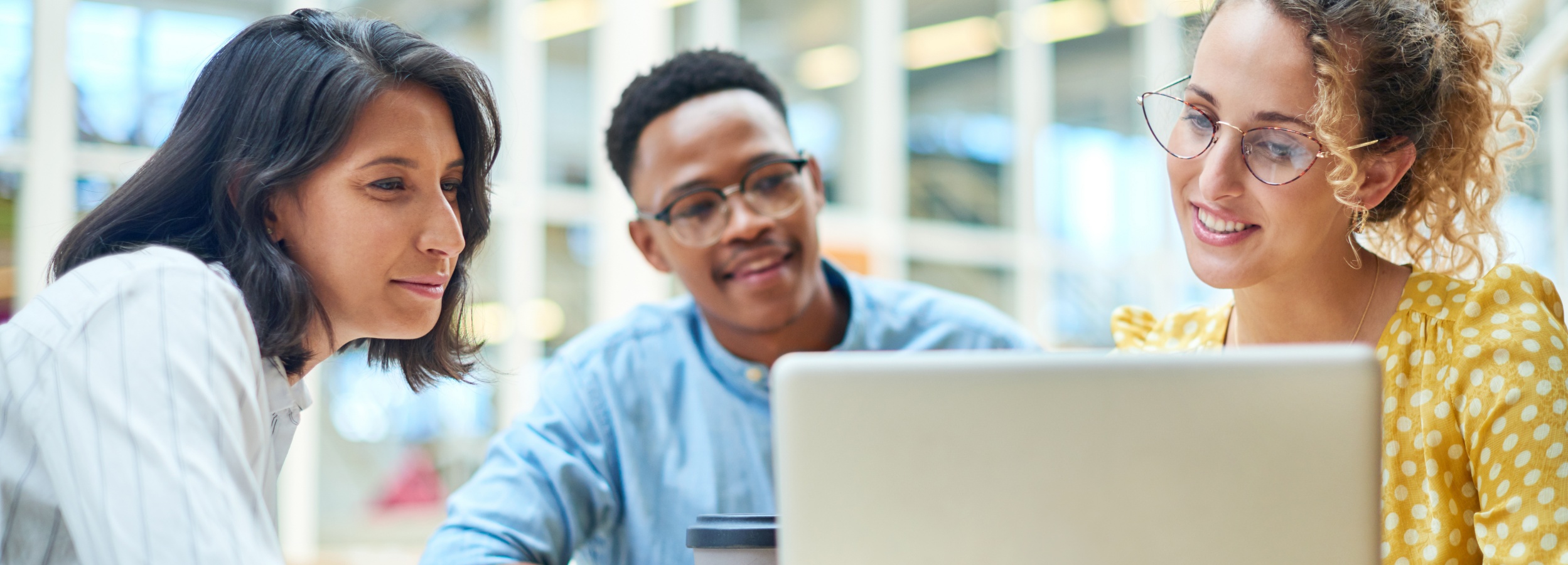 Das Bild zeigt eine fokussierte Zusammenarbeit dreier junger Erwachsener vor einem Laptop, die eine positive und produktive Atmosphäre ausstrahlt.

Das Bild zeigt drei Personen, wahrscheinlich Studenten oder junge Berufstätige, die sich um einen Laptop versammelt haben. Eine Frau mit dunklem, glattem Haar und einem hellen Hemd schaut aufmerksam auf den Laptop. Neben ihr ein junger Mann mit kurzen, dunklen Haaren und einer hellblauen Hose, der ebenfalls den Laptop fokussiert und dabei lächelt. Auf der anderen Seite des Laptops sitzt eine Frau mit lockigem, hellem Haar und einer gelben Bluse mit weißen Punkten. Sie trägt eine Brille und lächelt ebenfalls, während sie auf den Laptop schaut.

Im Hintergrund ist ein verschwommener Bereich mit Fenstern oder Glaspaneelen zu erkennen, was auf eine moderne Büro- oder Lernumgebung hindeutet. Auf dem Tisch vor dem Laptop steht ein Kaffeebecher, was die Szene noch entspannter und arbeitsfreundlicher wirken lässt. Die Stimmung ist positiv und kooperativ, was durch das Lächeln der Personen und ihre Körperhaltung verstärkt wird. Die Atmosphäre ist hell und einladend, was auf einen produktiven und angenehmen Arbeits- oder Lernort hindeutet.
