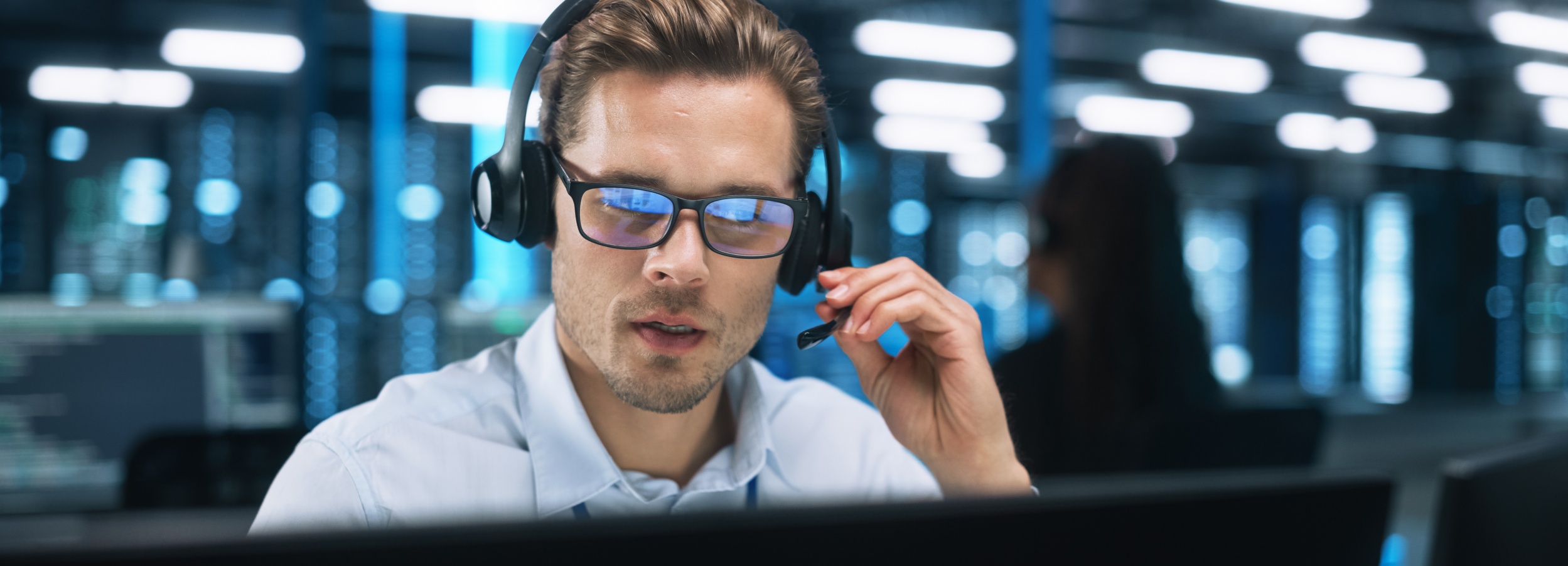 Ein Mann mit Brille und Headset sitzt in einem Serverraum und spricht.